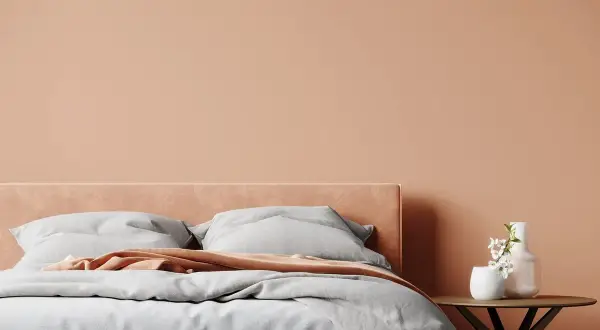 Lit douillet dans une chambre aux tons pêche, une belle idée couleur chambre adulte zen. Draps gris, plaid corail et vase fleuri sur table ronde.