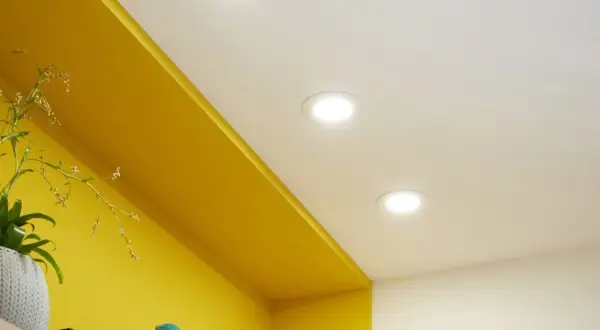Disposition de spots encastrés au plafond pour une ambiance lumineuse dans la chambre, éclairant joliment les étagères jaunes.