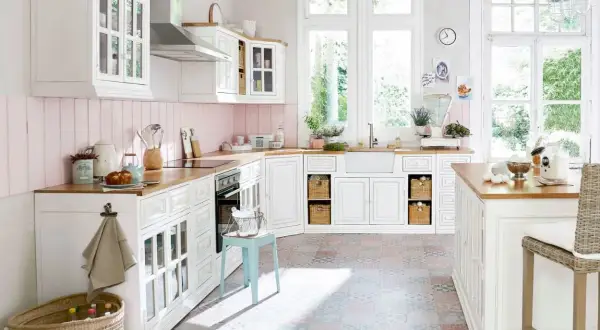Une cuisine blanche style campagne chic, lumineuse avec ses grandes fenêtres, son plan de travail en bois et son sol aux motifs colorés.