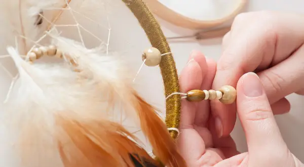 Mains assemblant un attrape-rêves, ajoutant des perles en bois pour une touche naturelle. Idées pour que faire avec des perles en bois.