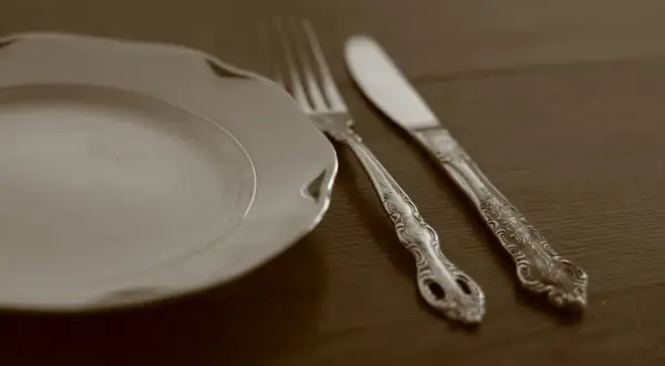 Une assiette blanche et des couverts en argent ornés, prêts pour un repas. Apprenez comment nettoyer des couverts en argent pour qu'ils brillent.
