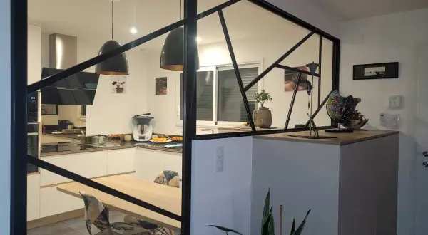 Une cuisine moderne avec une cloison lumineuse en verre et métal noir, séparant l'espace repas de la cuisine.