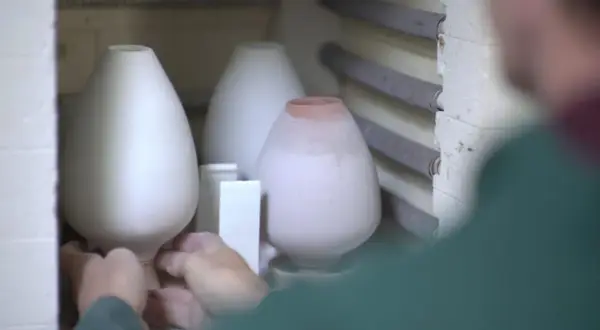 Mains plaçant délicatement des pièces de céramique au four pour leur cuisson.