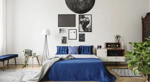 Chambre bleu nuit avec lit, coussins capitonnés, plaid gris, lampadaire, table de chevet et décoration murale.