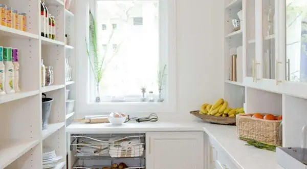 Arrière-cuisine blanche avec étagères remplies, fruits et légumes sur le comptoir.