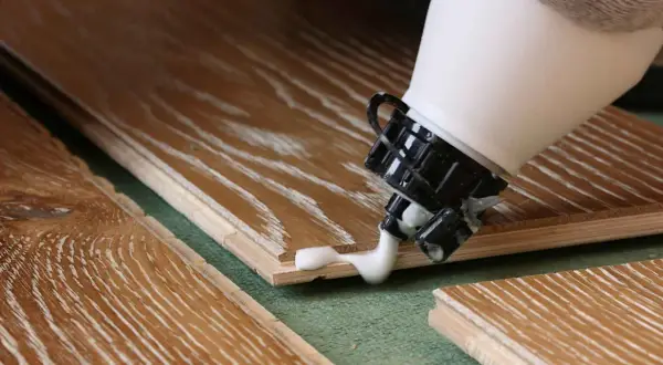 Application de colle à bois sur des lames de parquet. La colle blanche coule de l'embout d'une bouteille sur le bois.