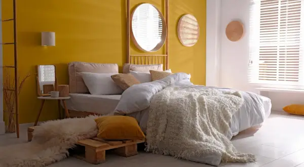 Chambre de fille avec mur jaune, lit blanc, tapis shaggy et miroir rond.