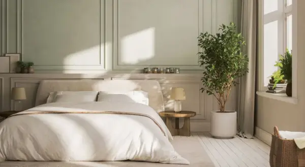 Chambre avec lit blanc, lambris vert pâle et plante verte.
