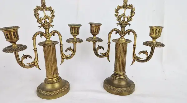 Deux candélabres en bronze doré, ornés de guirlandes et de cannelures, illustrent comment reconnaître un chandelier ancien par leur style et leur patine.