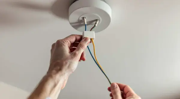 Mains électriques connectées pour installer un plafonnier. Les fils colorés sont manipulés avec soin.