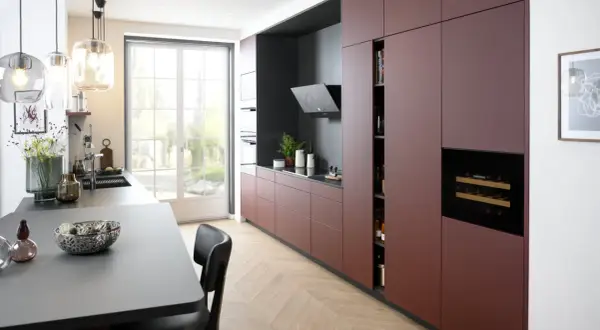 Cuisine moderne avec des armoires bordeaux allant jusqu'au plafond, un îlot central gris, et une grande fenêtre lumineuse.