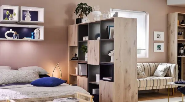 Chambre et salon séparés par une étagère modulable, avec lit douillet et canapé rayé.