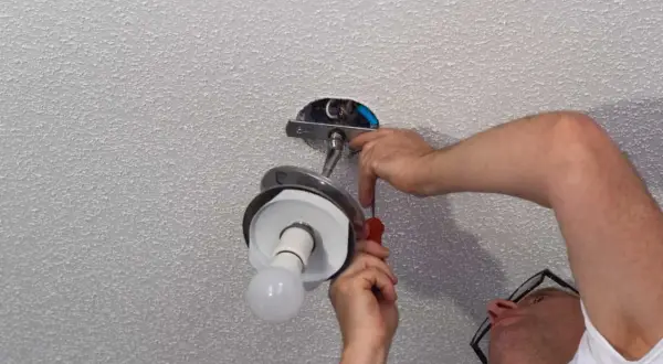 Un homme installe un lustre au plafond, utilisant un tournevis pour fixer le luminaire.