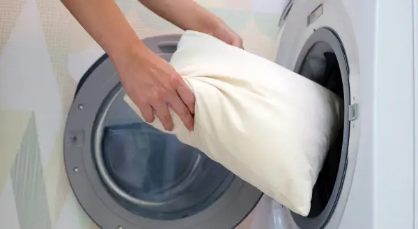 Une personne met un oreiller blanc dans une machine à laver.