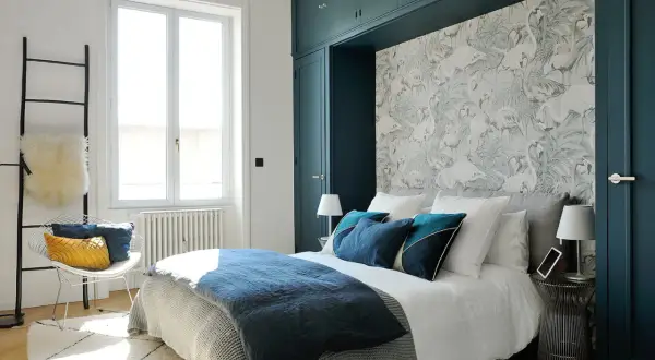 Chambre avec papier peint flamants roses, lit bleu marine et armoire vert foncé.