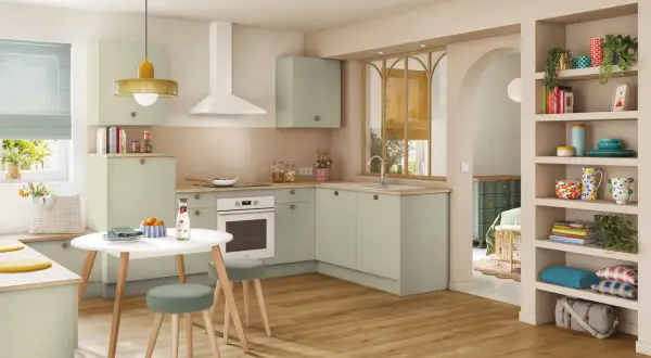 Cuisine moderne et colorée avec des meubles verts, une table ronde et des étagères décorées.