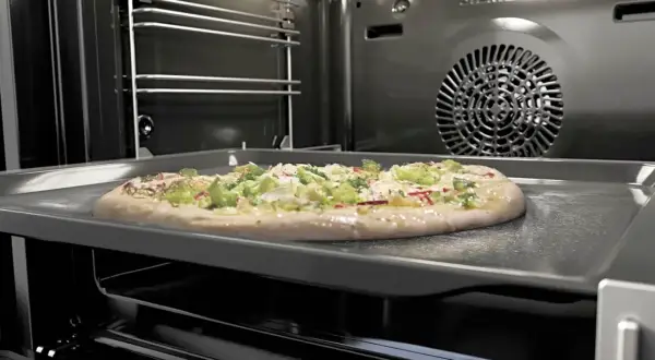 Une pizza garnie sur une plaque dans un four pyrolyse Siemens. La pizza est prête à être cuite.