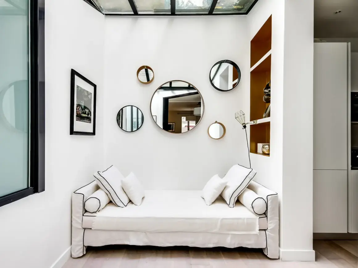 Plusieurs miroirs ronds de tailles variées sont accrochés sur un mur blanc au-dessus d'un canapé blanc.