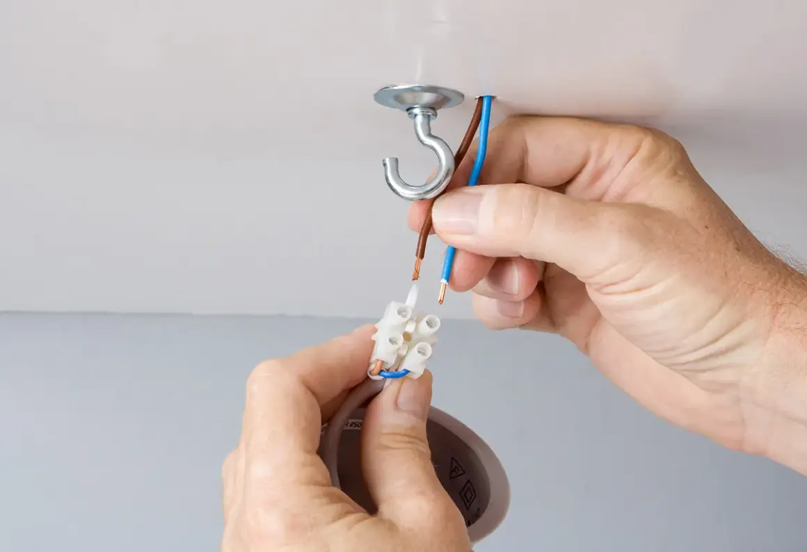 Mains électriques connectées pour changer un lustre. Un crochet au plafond supporte le nouveau luminaire.