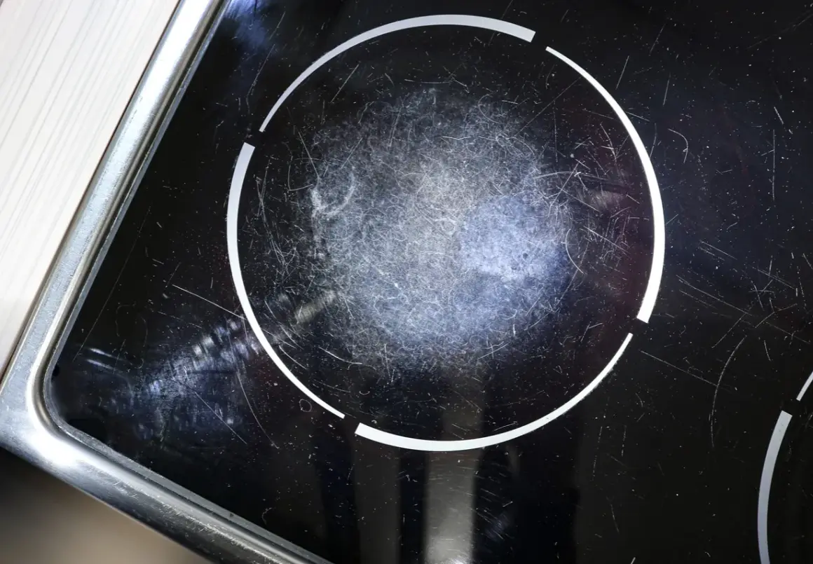 Gros plan sur une plaque à induction noire, marquée par de nombreuses rayures sur la zone de cuisson.
