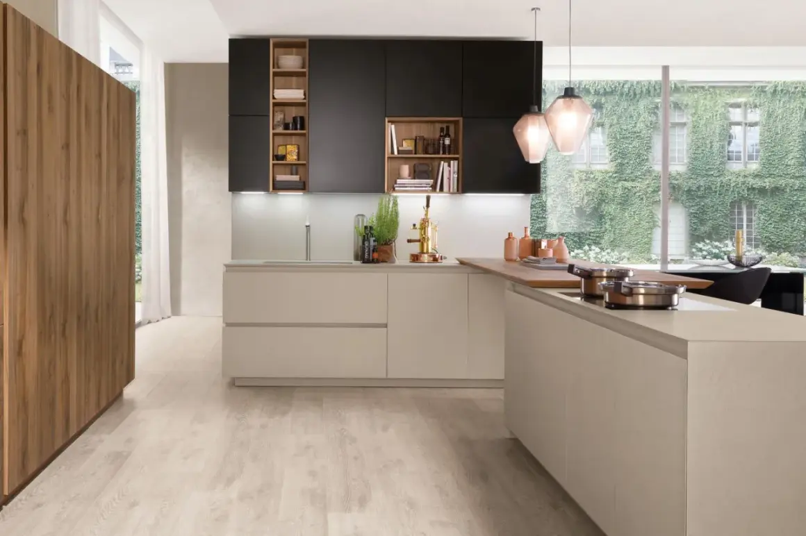 Cuisine moderne avec îlot central, armoires noires et bois, et grande fenêtre végétalisée.