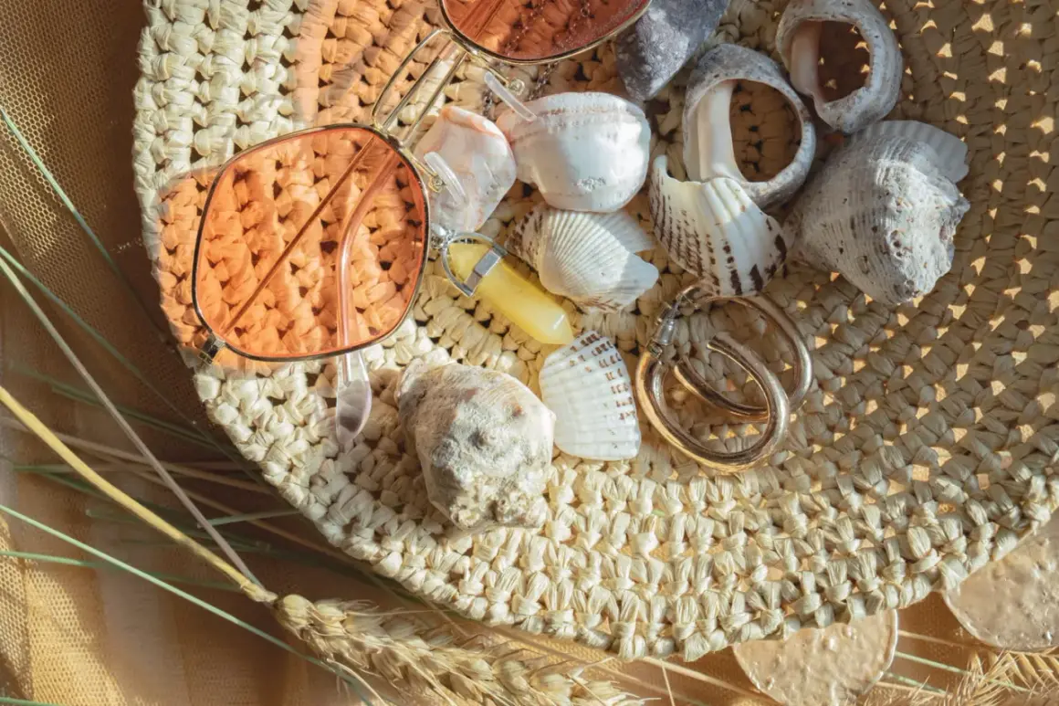 Lunettes de soleil roses, coquillages, bijoux et herbes sèches sur un chapeau de paille.