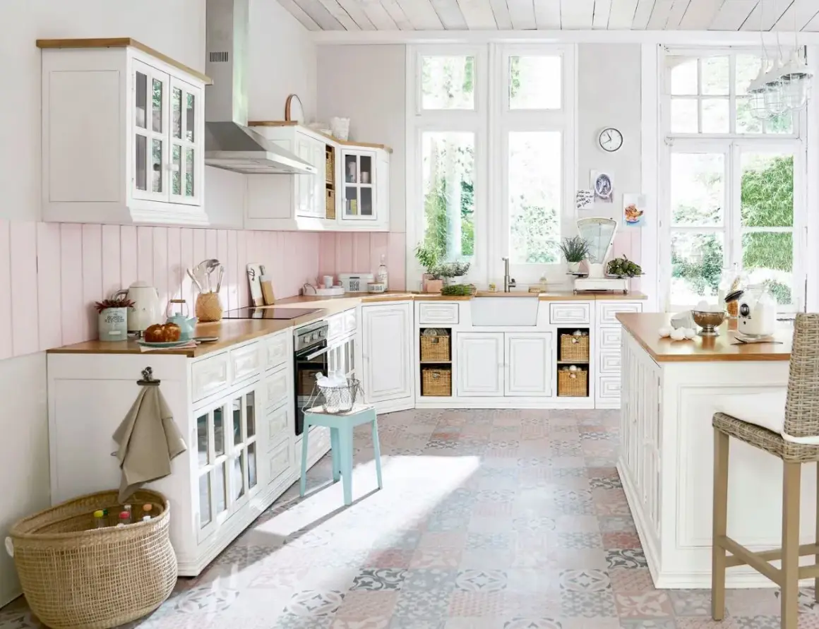 Une cuisine blanche style campagne chic, lumineuse avec ses grandes fenêtres, son plan de travail en bois et son sol aux motifs colorés.