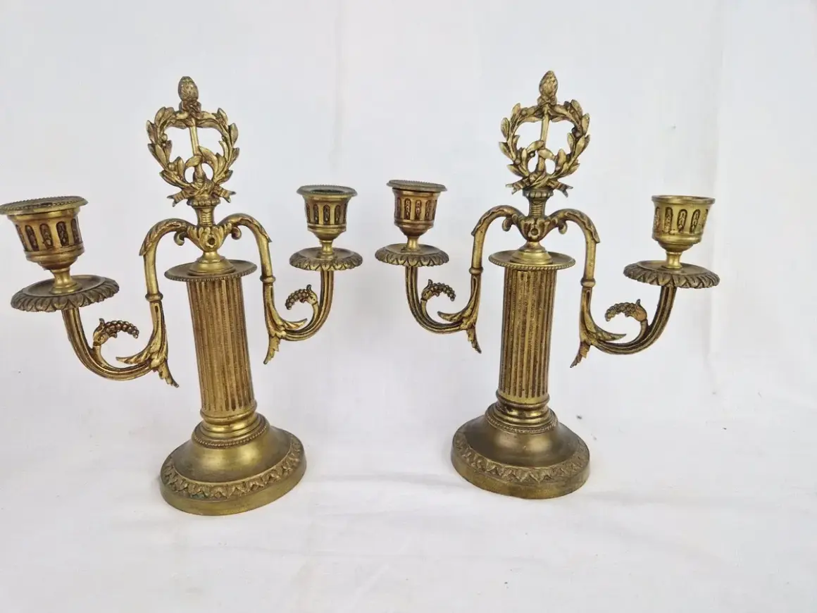 Deux candélabres en bronze doré, ornés de guirlandes et de cannelures, illustrent comment reconnaître un chandelier ancien par leur style et leur patine.