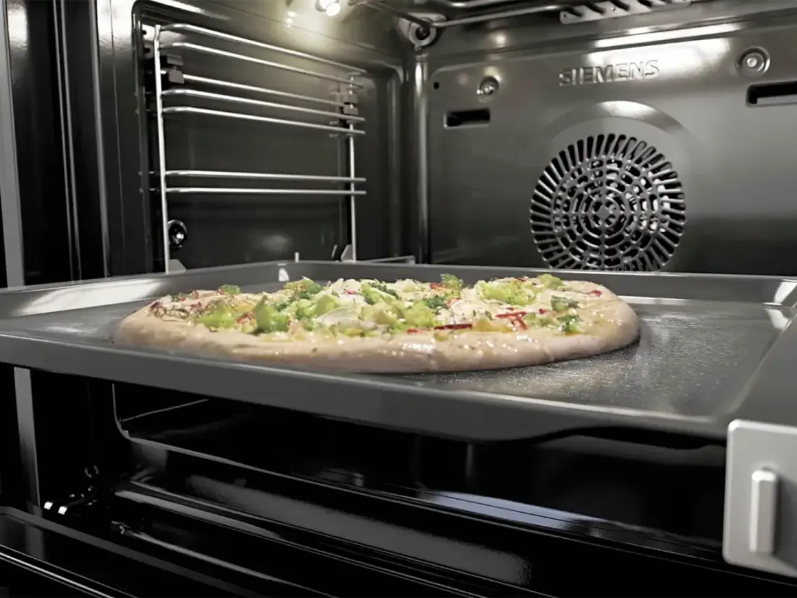 Une pizza garnie sur une plaque dans un four pyrolyse Siemens. La pizza est prête à être cuite.