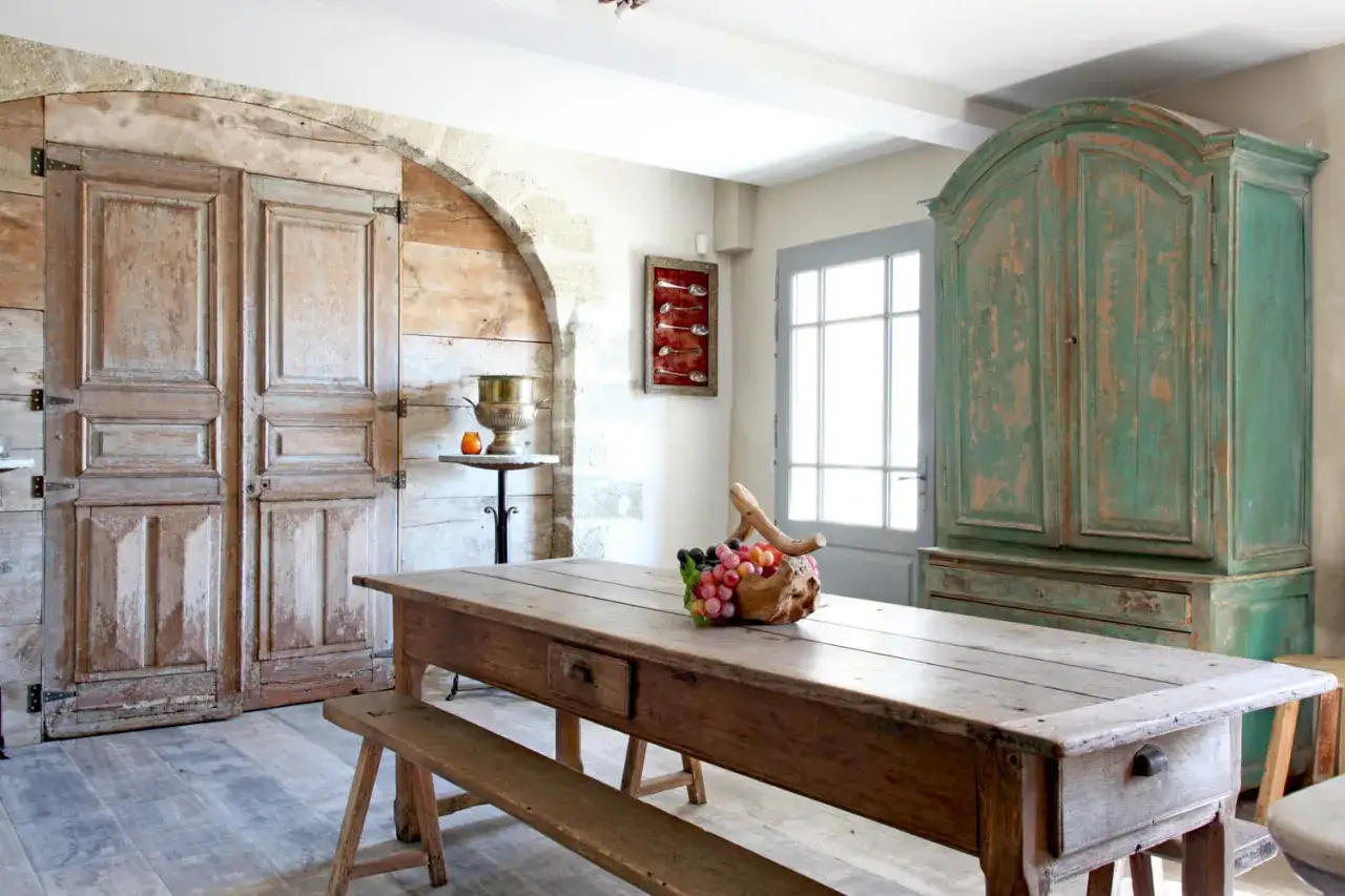 Une table rustique et un banc, parfaits pour patiner un meuble. Une grande armoire verte patin&eacute;e et des portes anciennes compl&egrave;tent ce d&eacute;cor champ&ecirc;tre.