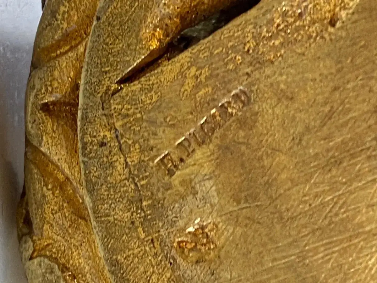Marquage sur un objet doré, peut-être une pièce pour comment reconnaître un chandelier ancien. Texture granuleuse et usée.