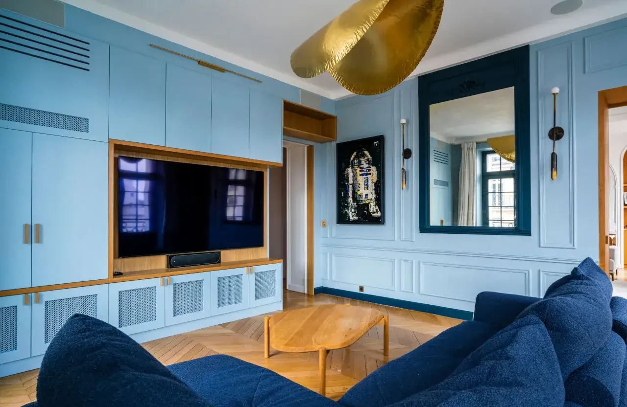 Salon moderne aux murs bleu couleur aqua, meuble TV intégré, canapé bleu nuit et table basse en bois.