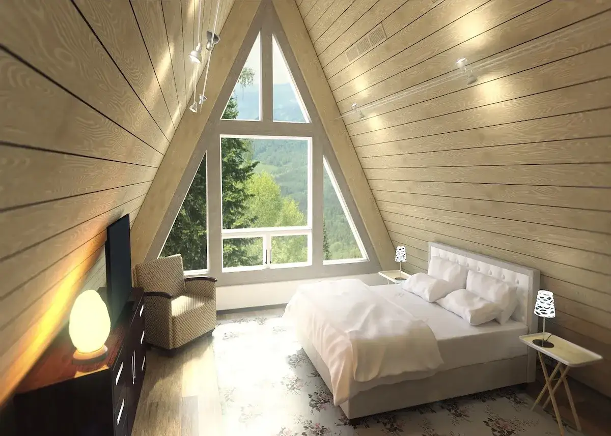 Chambre mansardée cocooning avec un grand triangle vitré offrant une vue sur la forêt. Un lit douillet, un fauteuil confortable et une lampe chaleureuse invitent à la détente.
