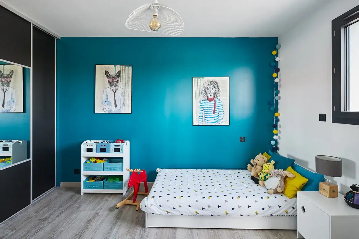 Chambre garçon : mur bleu vif, lit avec housse graphique, tableaux d'animaux stylisés. Une décoration tendance pour une chambre d'enfant pleine de vie.