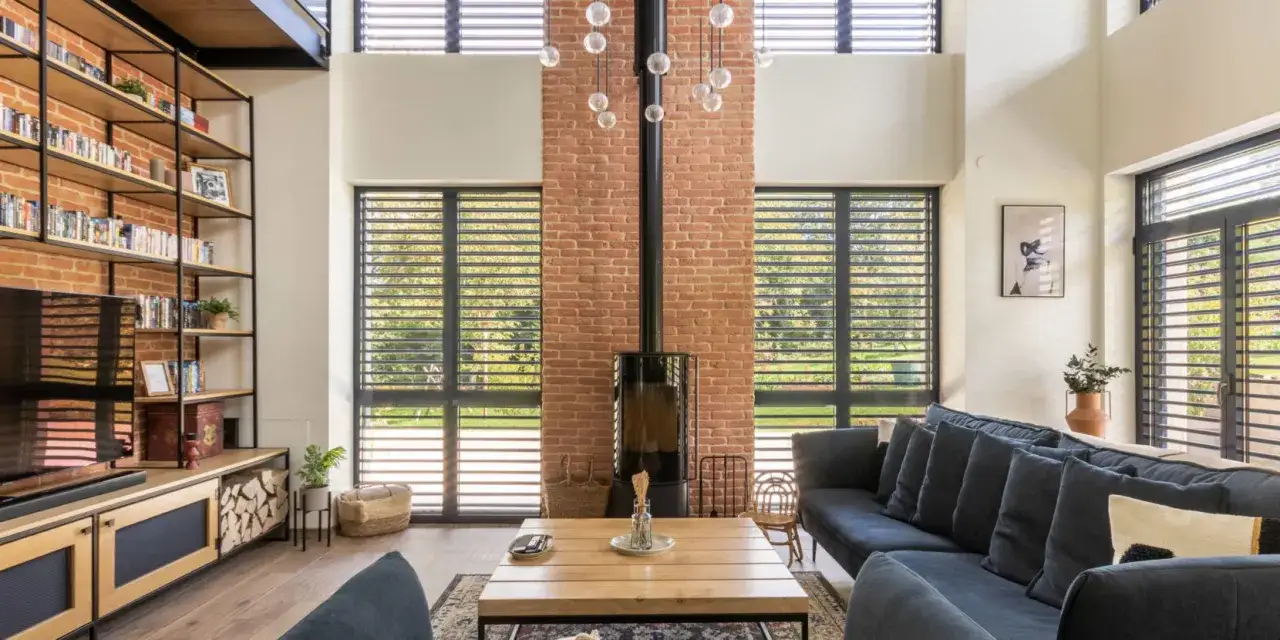 Salon au style industriel avec mur en briques apparentes, &eacute;tag&egrave;res m&eacute;talliques, po&ecirc;le noir et canap&eacute; bleu.
