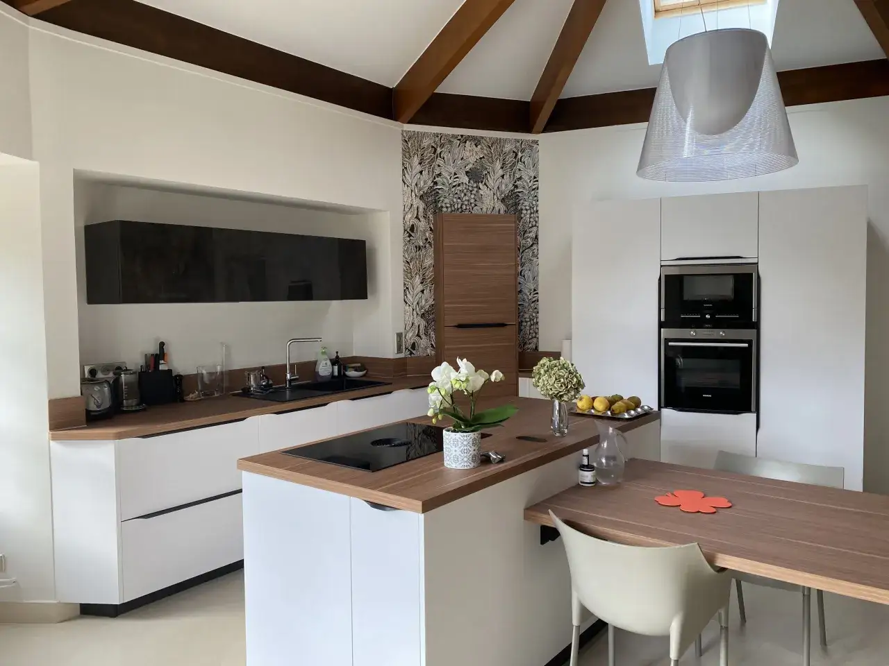 Cuisine moderne avec des meubles blancs et un cr&eacute;dence et plan de travail assortis en bois. Une table en bois avec des chaises claires est install&eacute;e.