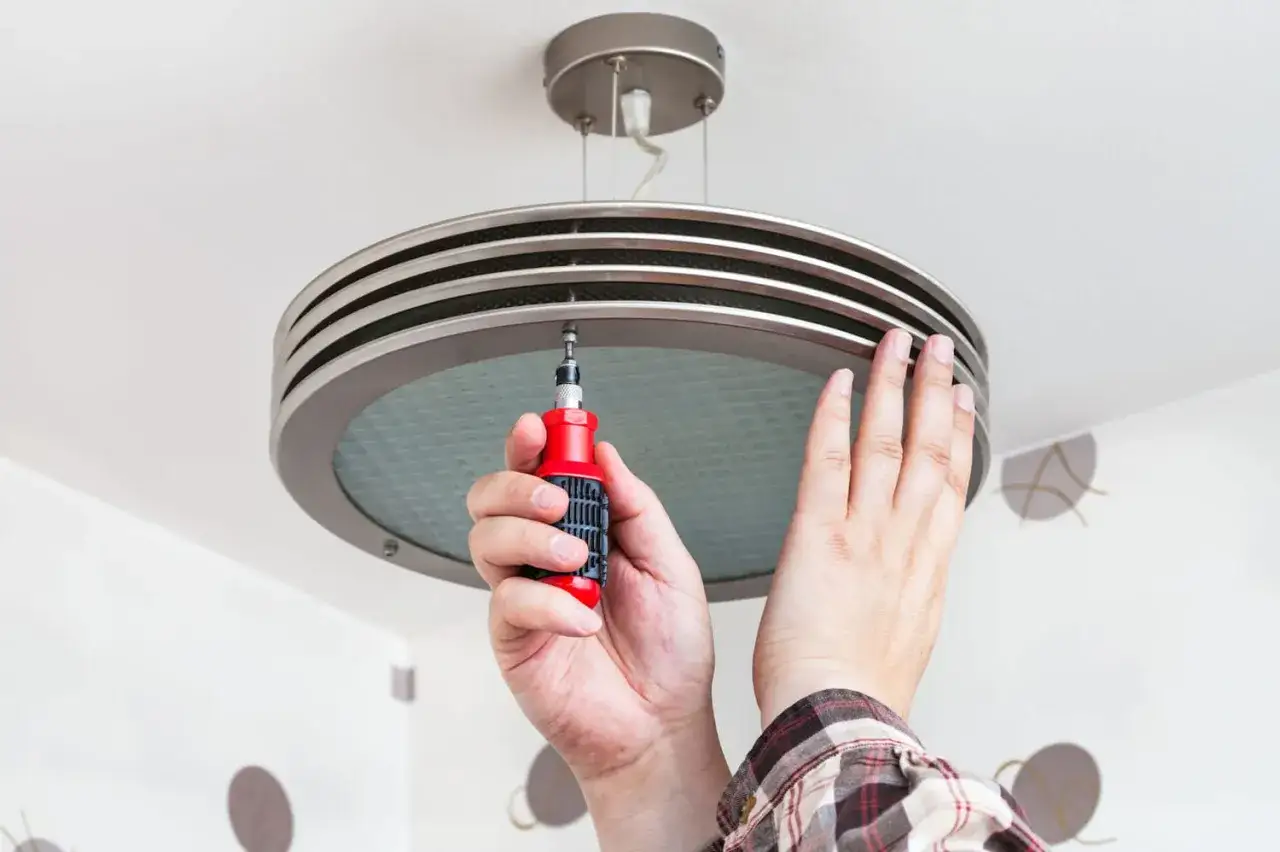 Installation d'une suspension moderne au plafond. Une main tient un tournevis pour fixer le luminaire, remplaçant ainsi un ancien spot.