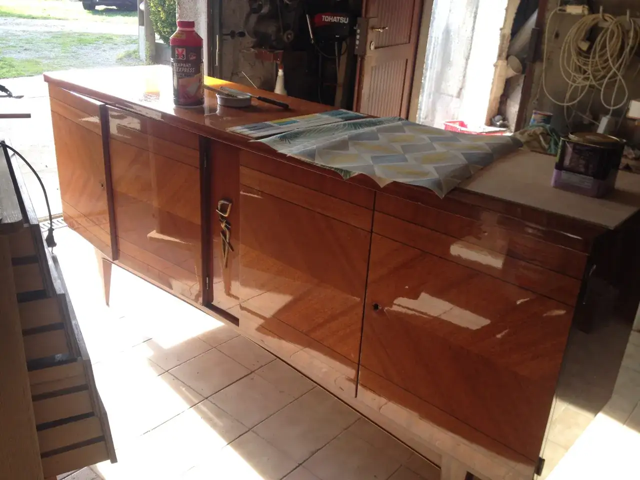 Préparation pour poncer un meuble vernis : un décapant et des outils sont prêts sur le buffet en bois.