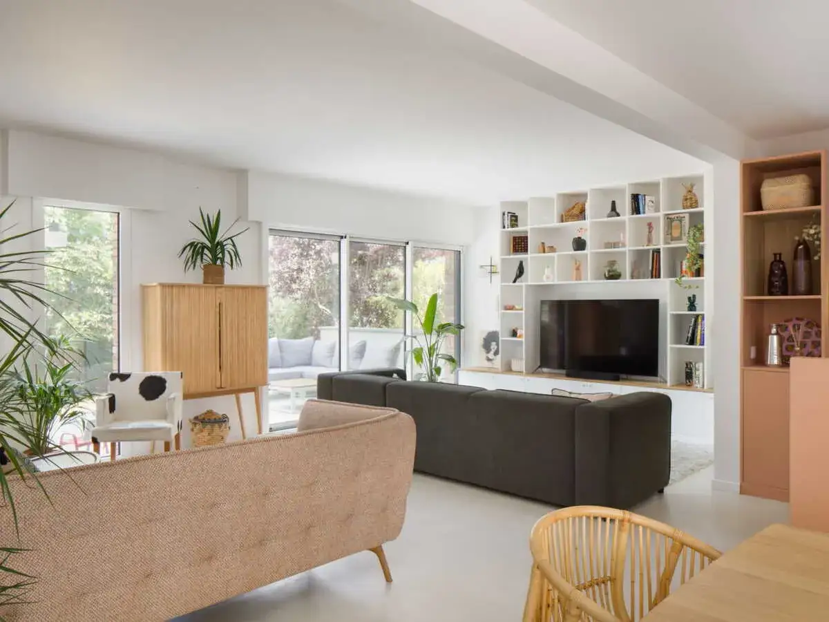 Un salon moderne avec deux canapés face à face, une TV intégrée dans une bibliothèque blanche et des plantes vertes.