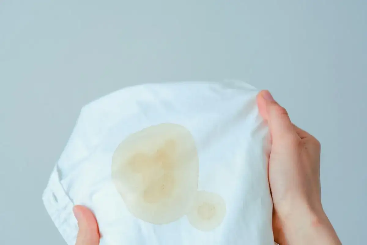 Mains tenant un tissu blanc avec une tache de gras. Une solution pour enlever tache de gras sur tissu est n&eacute;cessaire.