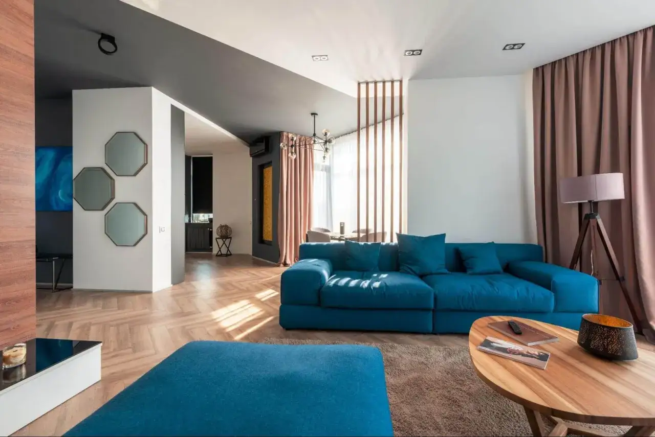 Un salon moderne avec un canapé bleu vif, un pouf assorti et une cloison lumineuse en bois créant une séparation élégante.