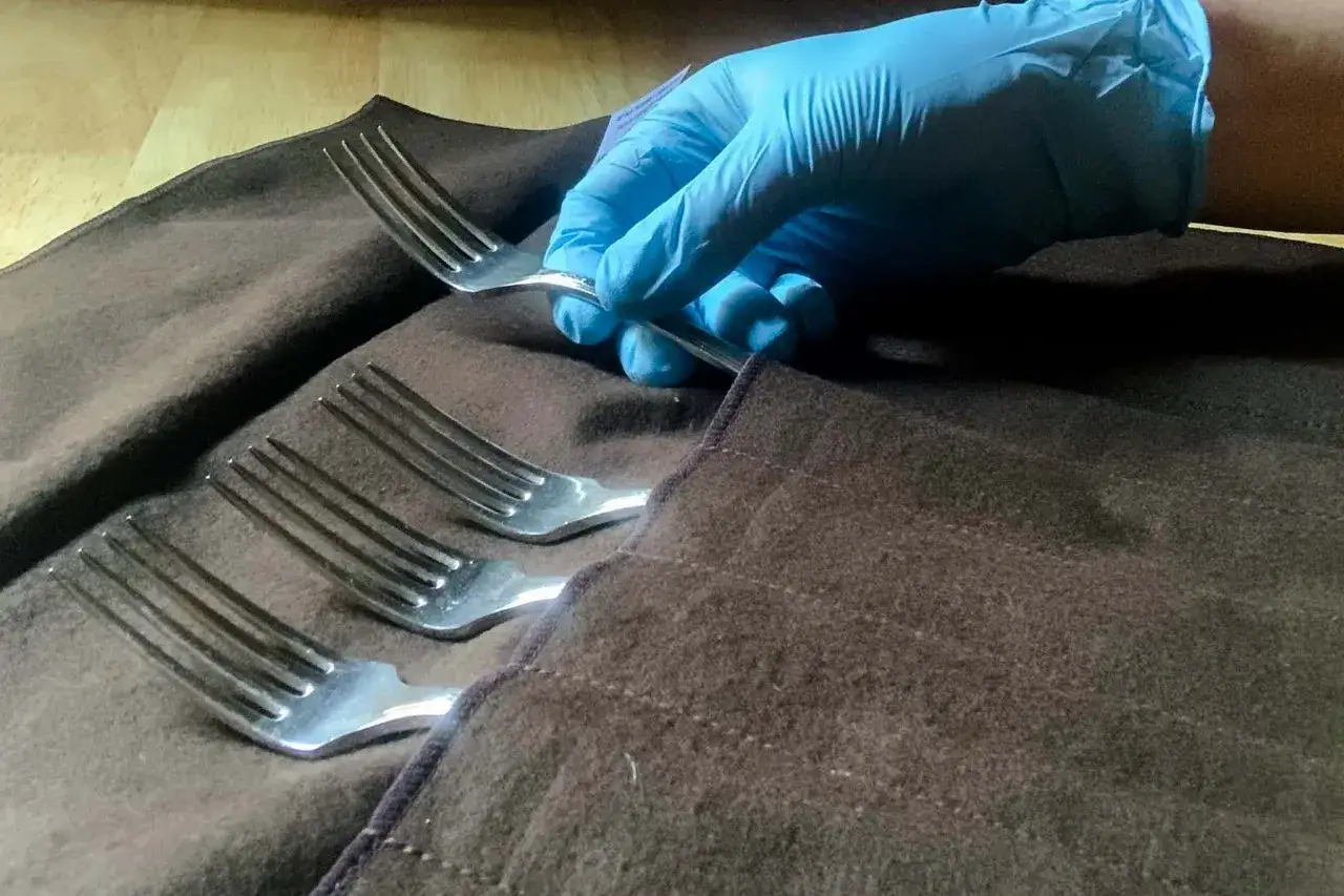 Maintenant, apprenons comment nettoyer des couverts en argent. Une main gant&eacute;e saisit une fourchette sur un tissu brun.