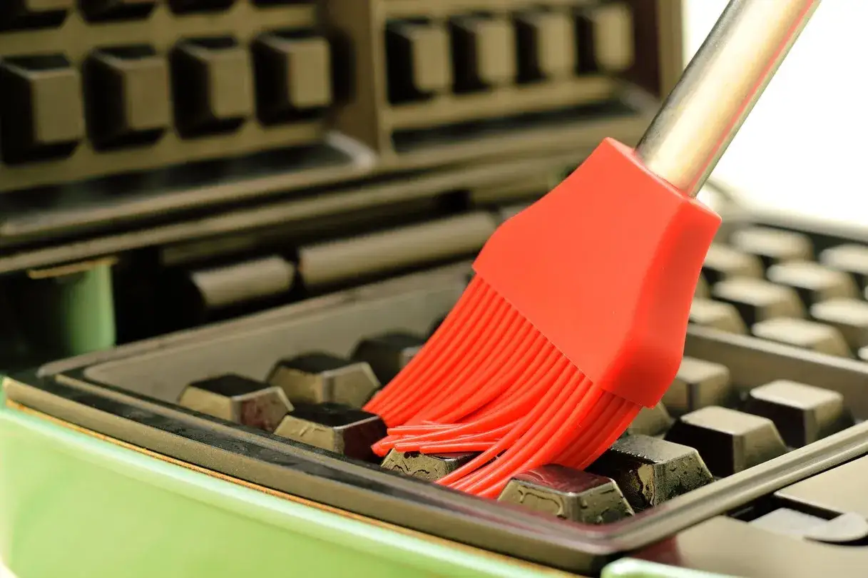 Un pinceau rouge nettoie les alv&eacute;oles d'un gaufrier vert. Astuce pour comment nettoyer un gaufrier.