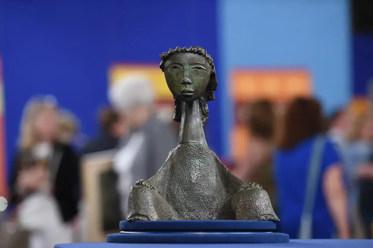 Un objet en bronze, une sculpture stylis&eacute;e d'un visage, semble &ecirc;tre une pi&egrave;ce de grande valeur, expos&eacute;e devant un public flou.