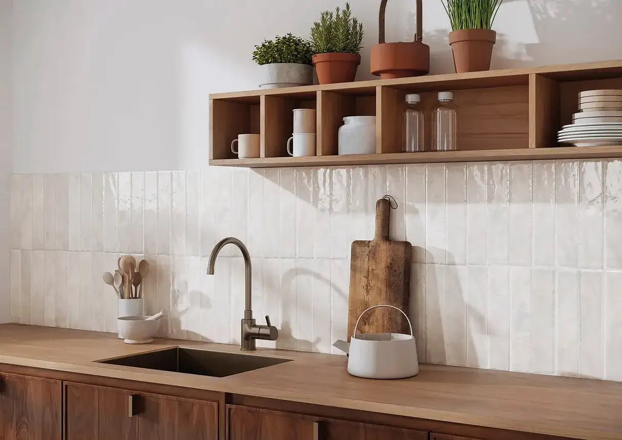 Cuisine blanche avec crédence zellige texturée. Évier, robinetterie moderne, plan de travail en bois, et étagères en bois avec des objets décoratifs.