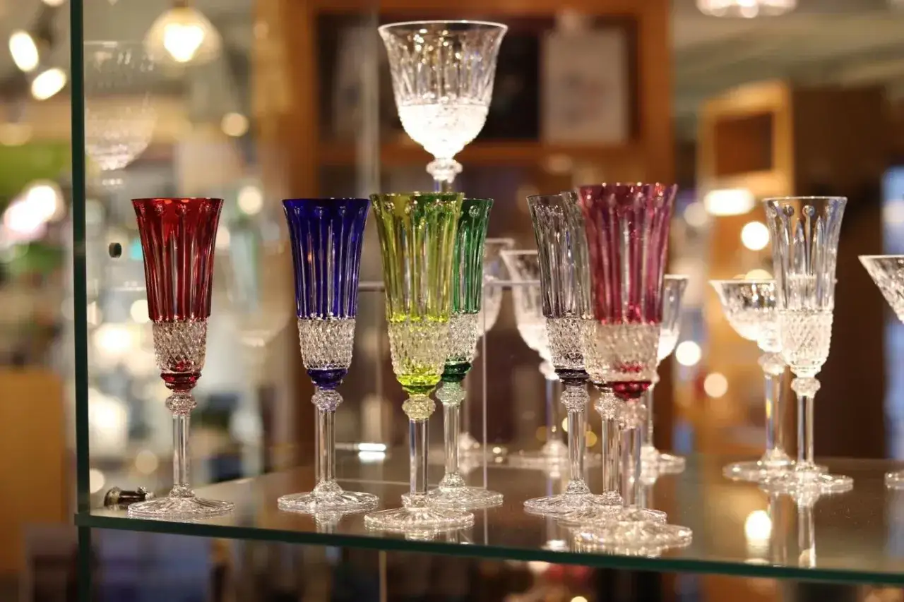 Comment reconnaitre du cristal : des verres colorés aux pieds taillés, brillants et transparents, exposés sur une étagère en verre.
