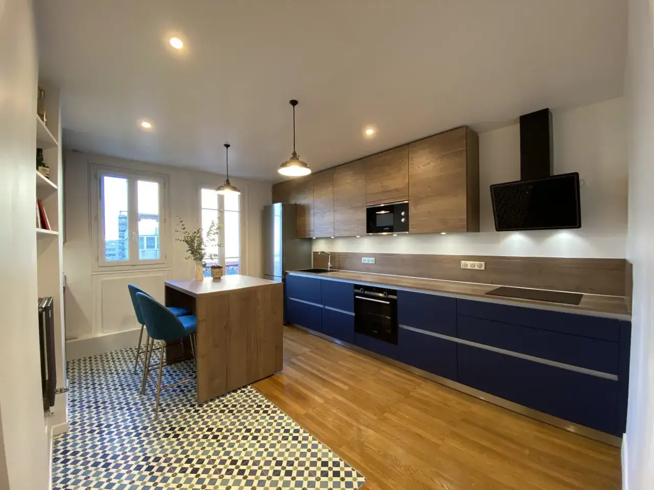 Cuisine bleu nuit et bois, avec un &icirc;lot central, des meubles hauts en bois et des meubles bas bleus. Le sol est un m&eacute;lange de parquet et de carrelage g&eacute;om&eacute;trique.