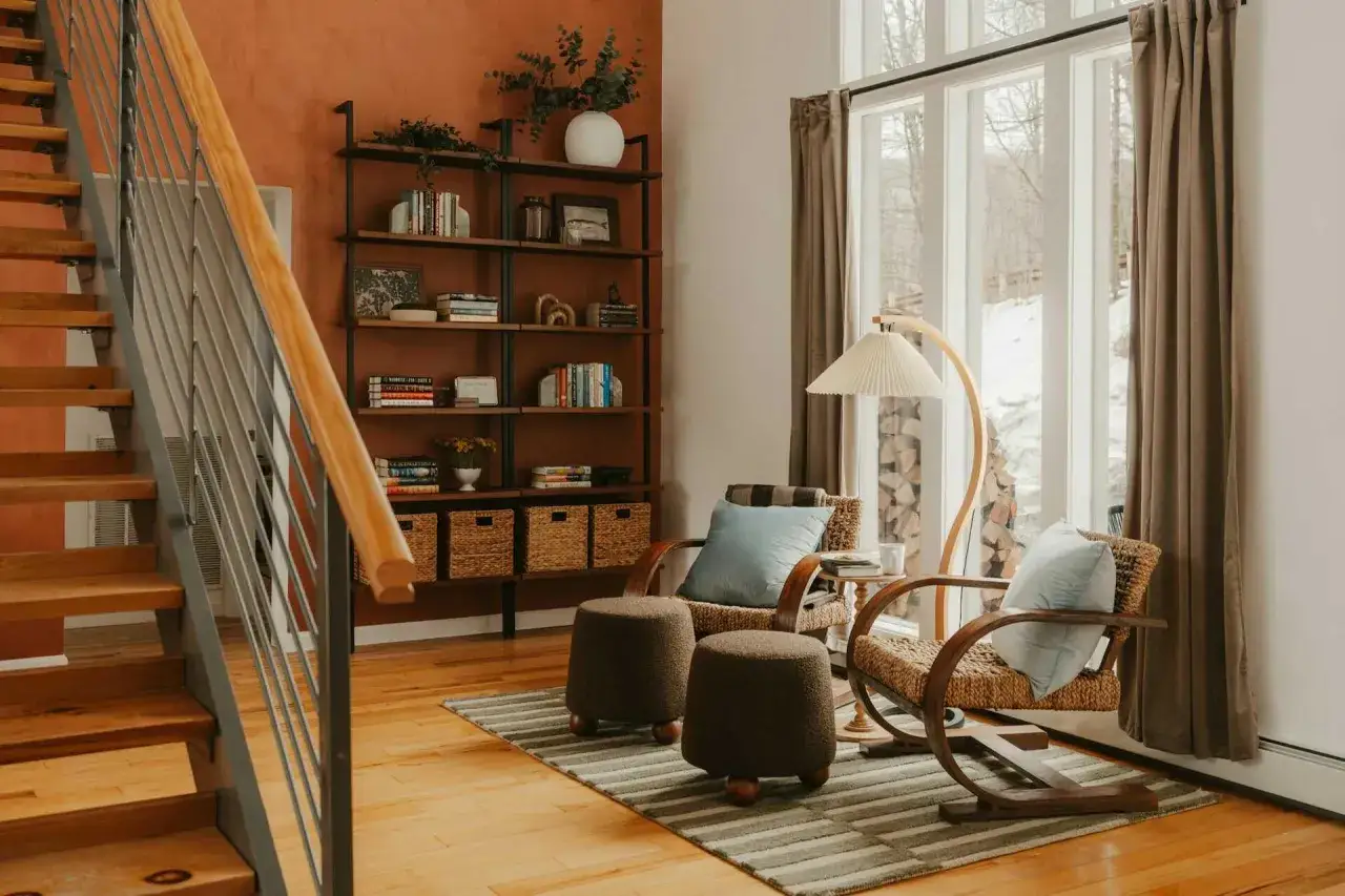 Un coin lecture zen avec fauteuils en rotin, poufs douillets, étagères remplies de livres et une grande fenêtre offrant une vue sur la nature enneigée.