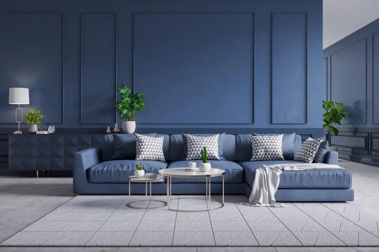 Salon moderne aux murs bleu paon, avec un canapé d'angle confortable, des coussins graphiques et des plantes vertes.