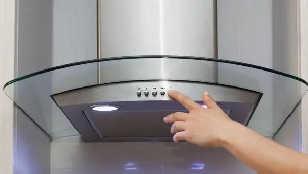 Main d'une personne appuyant sur le bouton d'une hotte recyclage ou évacuation moderne en acier inoxydable avec un éclairage intégré.